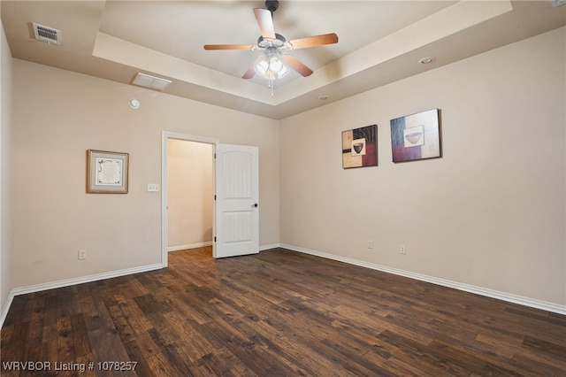 unfurnished room with a tray ceiling, ceiling fan, and dark wood-type flooring