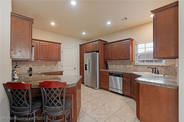 kitchen featuring a kitchen breakfast bar, sink, light tile patterned floors, kitchen peninsula, and stainless steel appliances