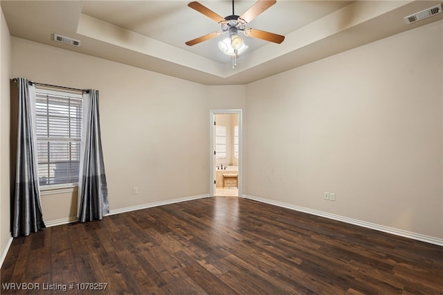 spare room with a raised ceiling, ceiling fan, and dark wood-type flooring