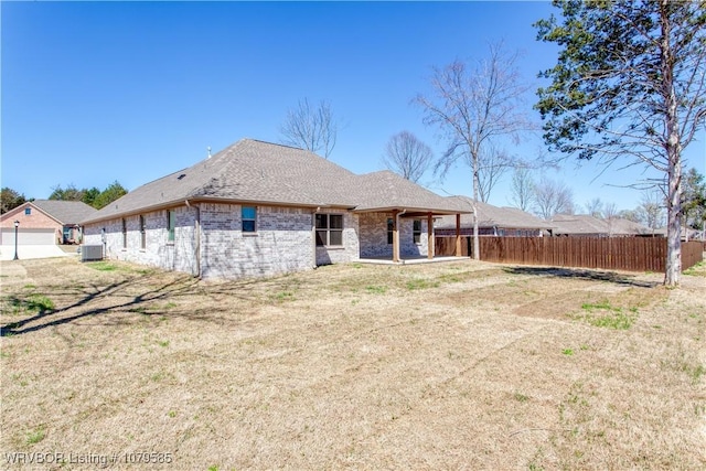 rear view of property featuring brick siding, fence, and roof with shingles