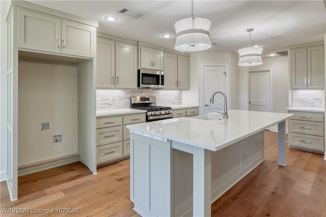 kitchen featuring visible vents, appliances with stainless steel finishes, a sink, an island with sink, and light wood-type flooring