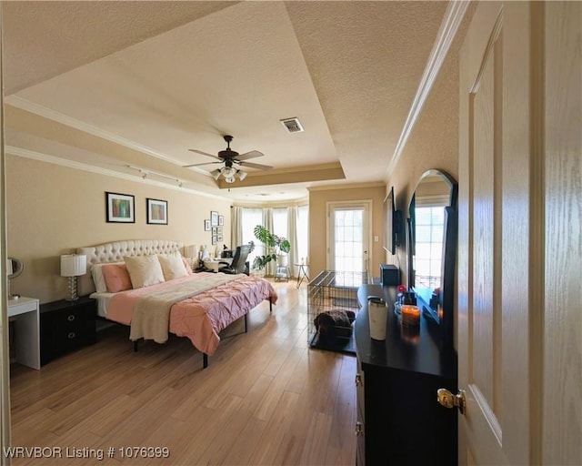 bedroom with hardwood / wood-style floors, crown molding, ceiling fan, a textured ceiling, and a tray ceiling