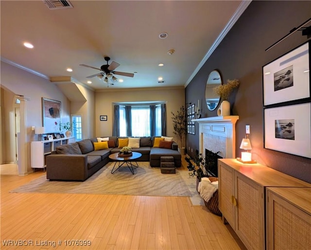 living room with ceiling fan, ornamental molding, light hardwood / wood-style flooring, and a tiled fireplace