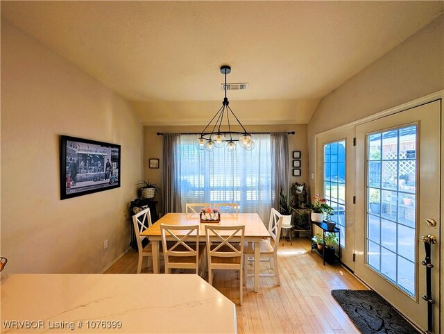 dining area featuring a notable chandelier, light hardwood / wood-style flooring, and vaulted ceiling