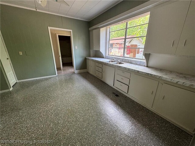 kitchen featuring a sink, wooden walls, light countertops, white cabinets, and baseboards