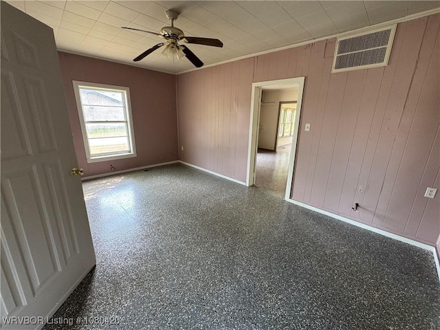 spare room with wooden walls, visible vents, baseboards, and ceiling fan