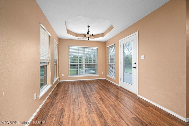 interior space with a tray ceiling, wood finished floors, an inviting chandelier, and baseboards