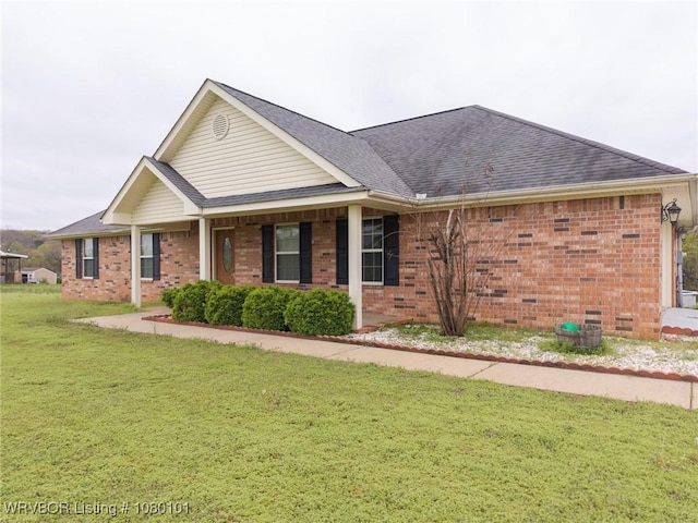 view of front facade featuring roof with shingles, a front yard, and brick siding