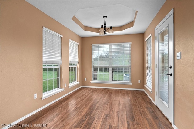 empty room featuring wood finished floors, baseboards, an inviting chandelier, and a raised ceiling