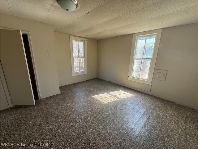 empty room featuring a paneled ceiling and baseboards