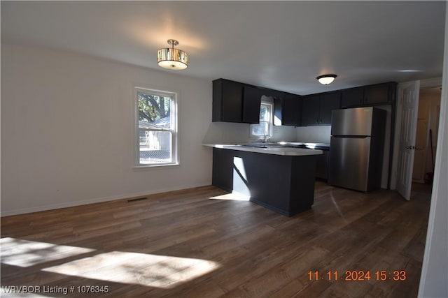 kitchen with stainless steel refrigerator, sink, dark hardwood / wood-style flooring, kitchen peninsula, and decorative light fixtures