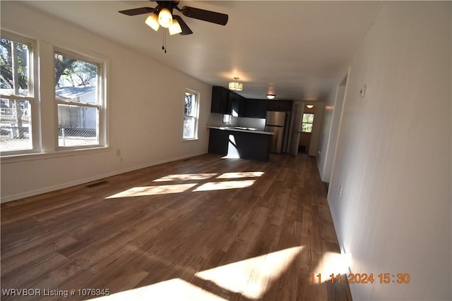 unfurnished living room with ceiling fan, a healthy amount of sunlight, and dark wood-type flooring