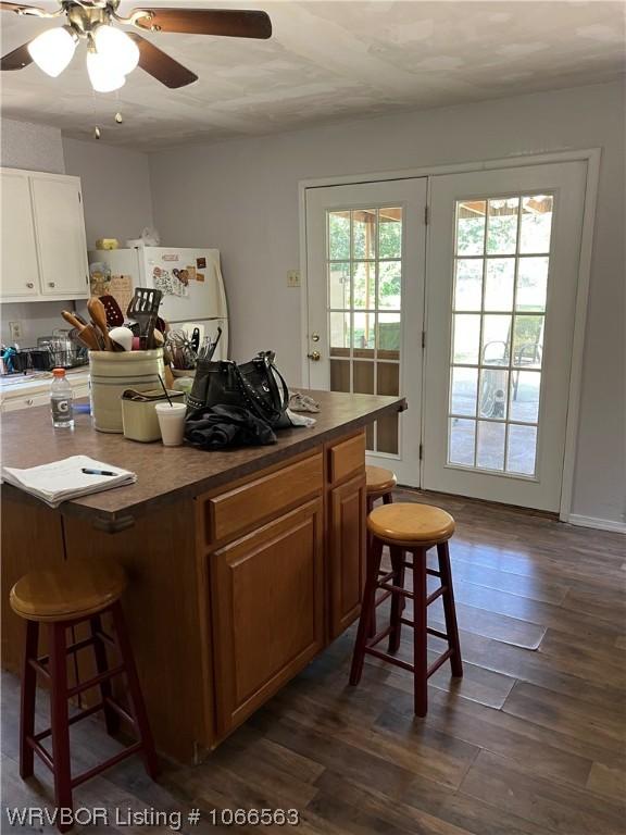 kitchen with a breakfast bar area, white cabinetry, ceiling fan, and dark wood-type flooring