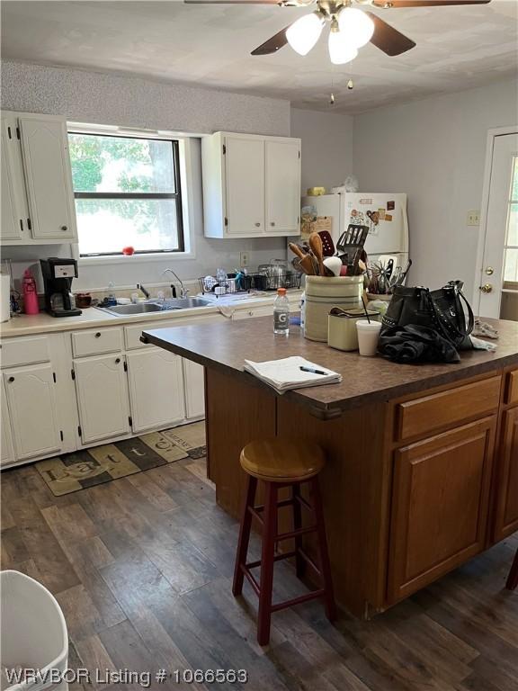 kitchen with a kitchen breakfast bar, ceiling fan, sink, dark hardwood / wood-style floors, and white cabinetry