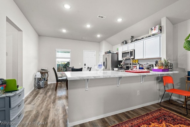 kitchen featuring a breakfast bar area, wood finished floors, a peninsula, stainless steel appliances, and white cabinets