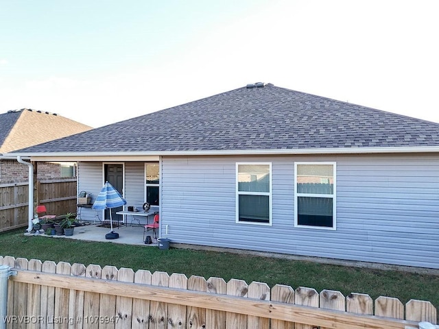 rear view of house with fence, a lawn, a patio area, and roof with shingles
