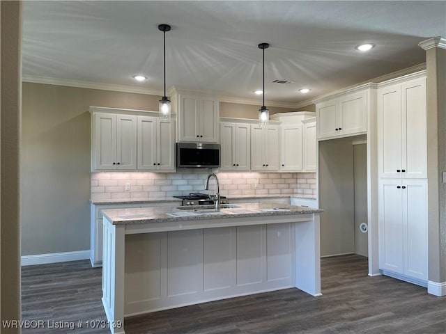 kitchen with white cabinets, decorative light fixtures, light stone counters, and an island with sink