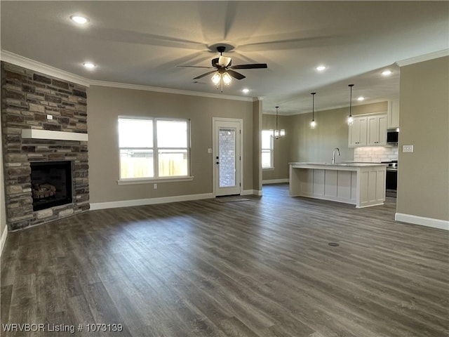 unfurnished living room with a stone fireplace, ceiling fan, sink, and dark wood-type flooring