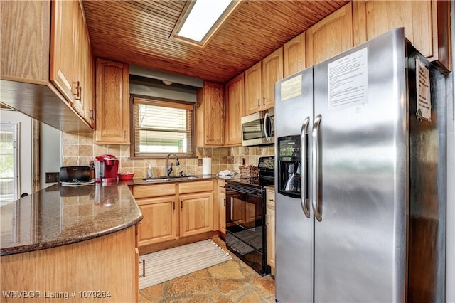 kitchen with a sink, appliances with stainless steel finishes, backsplash, dark stone counters, and stone finish floor