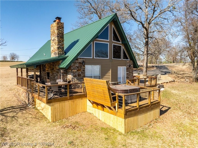 rear view of house featuring stone siding, metal roof, a chimney, and a wooden deck