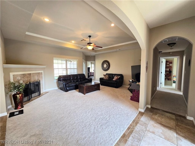 living room with light carpet, a raised ceiling, ceiling fan, and a tiled fireplace