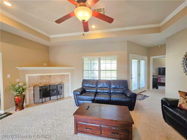 living room featuring crown molding, ceiling fan, a tray ceiling, light colored carpet, and a tiled fireplace