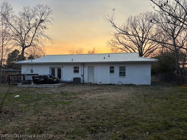 back of property at dusk featuring metal roof, central AC unit, and a lawn