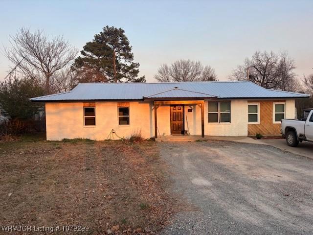 ranch-style house with metal roof, driveway, and stucco siding