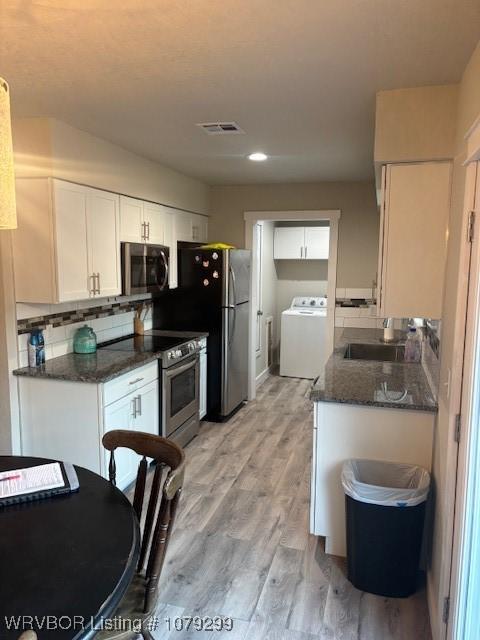 kitchen featuring light wood finished floors, stainless steel appliances, visible vents, a sink, and washer / dryer