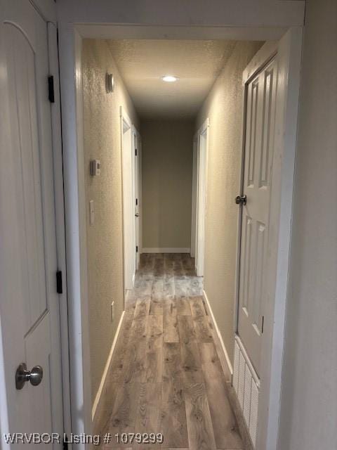 hallway featuring a textured wall, light wood-style flooring, and baseboards