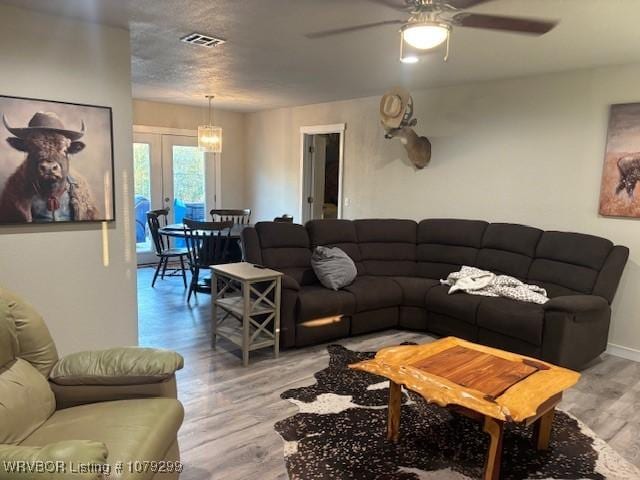 living room featuring french doors, visible vents, light wood-style flooring, a ceiling fan, and a textured ceiling