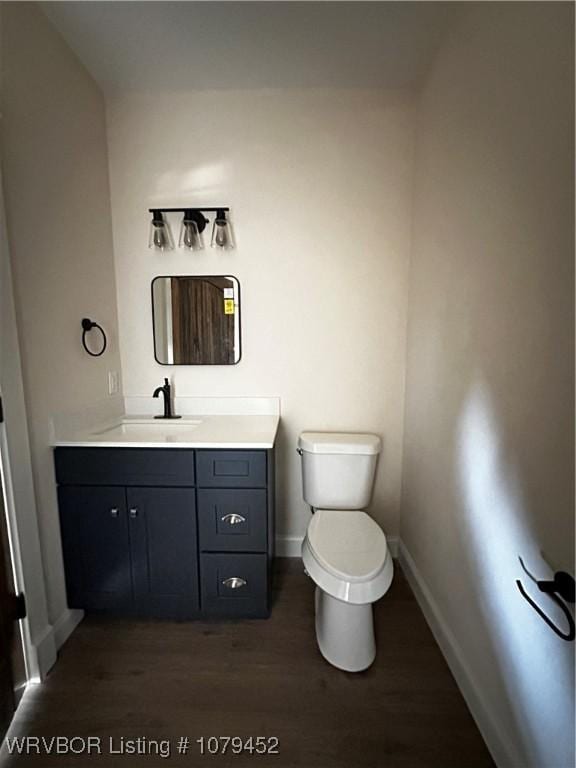 half bathroom with baseboards, vanity, toilet, and wood finished floors