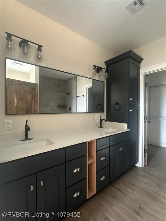 full bath with double vanity, visible vents, a sink, and wood finished floors