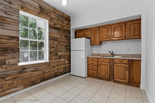 kitchen with freestanding refrigerator, a sink, wooden walls, brown cabinetry, and light countertops