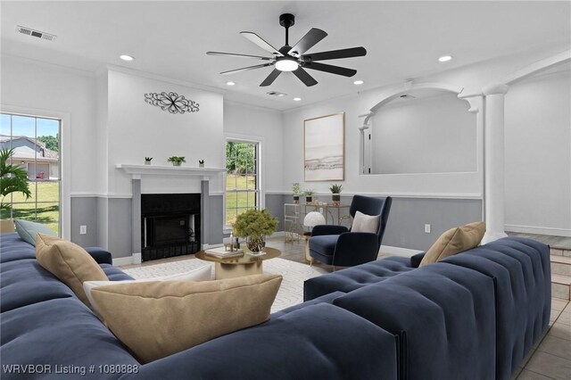 living area with healthy amount of natural light, a ceiling fan, a glass covered fireplace, crown molding, and light tile patterned floors