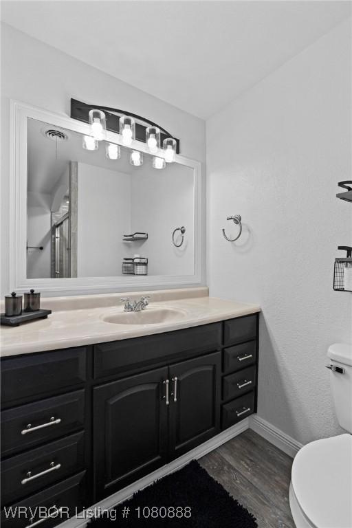 bathroom featuring toilet, vanity, wood finished floors, and baseboards