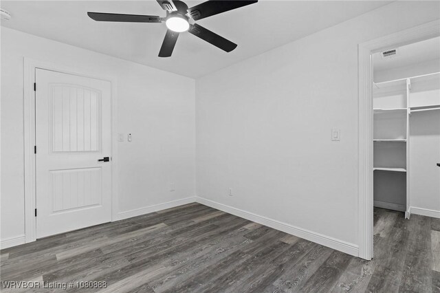 unfurnished bedroom featuring dark wood-style flooring, a walk in closet, a closet, baseboards, and a ceiling fan