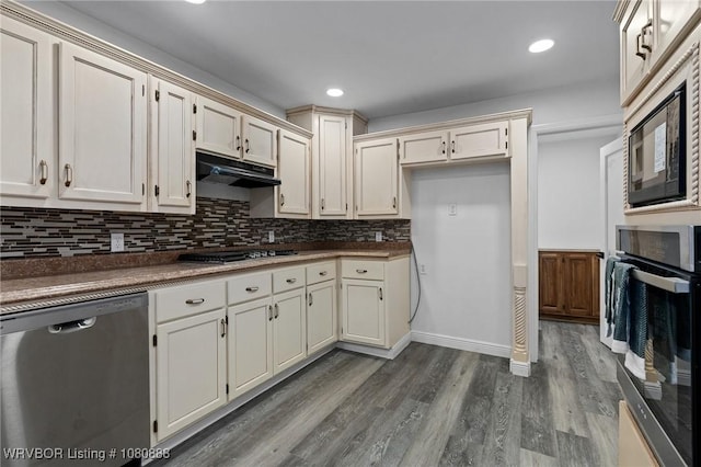 kitchen featuring appliances with stainless steel finishes, under cabinet range hood, dark countertops, dark wood finished floors, and recessed lighting