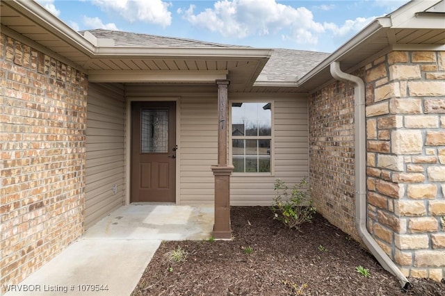 doorway to property with stone siding, brick siding, and a shingled roof