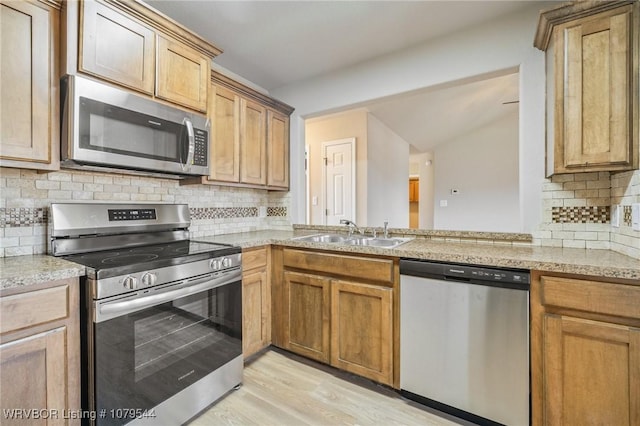 kitchen with light wood-style flooring, a sink, a peninsula, appliances with stainless steel finishes, and light countertops