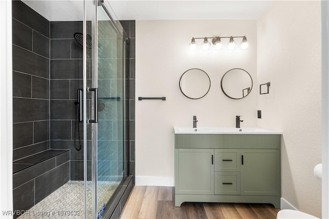 full bath with a stall shower, a sink, wood finished floors, double vanity, and baseboards