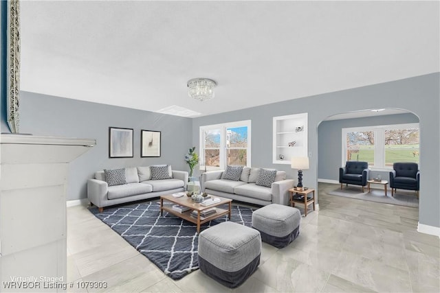 living room featuring arched walkways, baseboards, a chandelier, and built in features