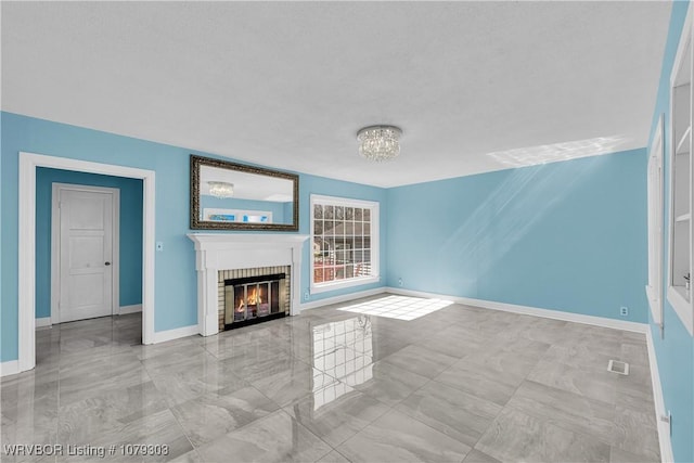 unfurnished living room with a notable chandelier, a brick fireplace, visible vents, and baseboards