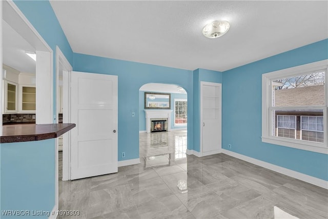 unfurnished bedroom with marble finish floor, a glass covered fireplace, and baseboards