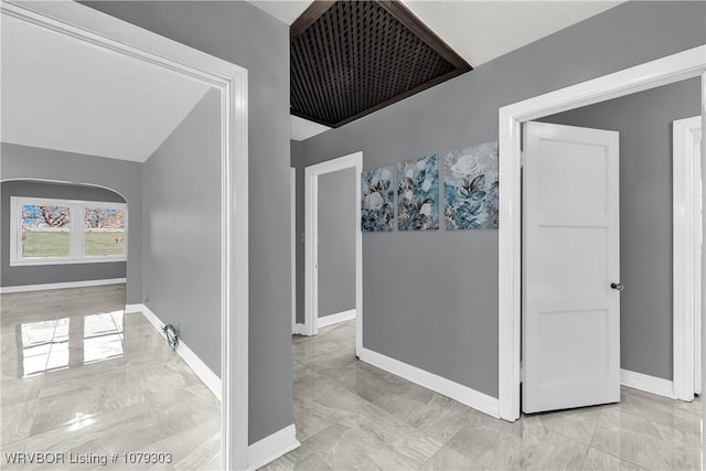 hall featuring arched walkways, marble finish floor, and baseboards