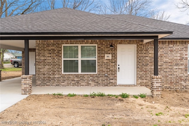 view of front of home with an attached carport, brick siding, roof with shingles, and driveway