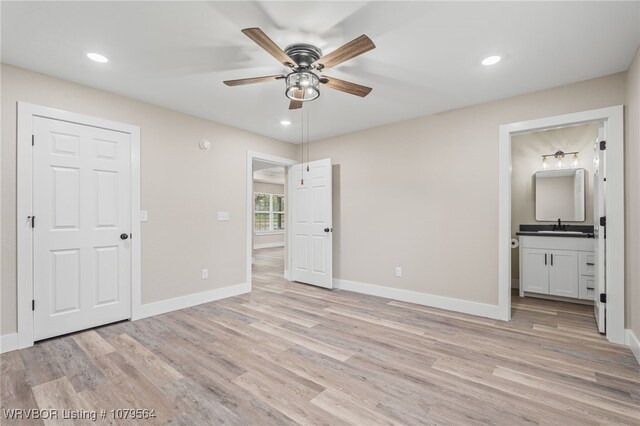 unfurnished bedroom with baseboards, ensuite bathroom, a sink, and light wood-type flooring