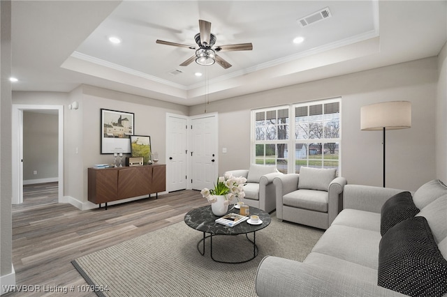 living room with a tray ceiling, visible vents, wood finished floors, and a ceiling fan