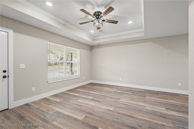 empty room featuring baseboards, crown molding, wood finished floors, and a raised ceiling