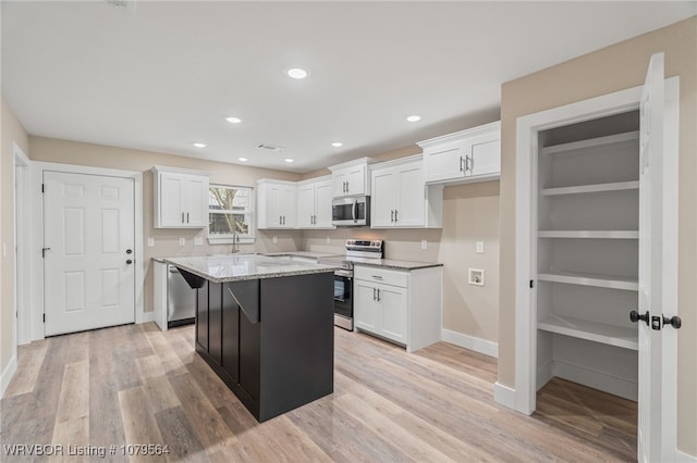 kitchen featuring white cabinets, light wood finished floors, stainless steel appliances, light stone counters, and a center island